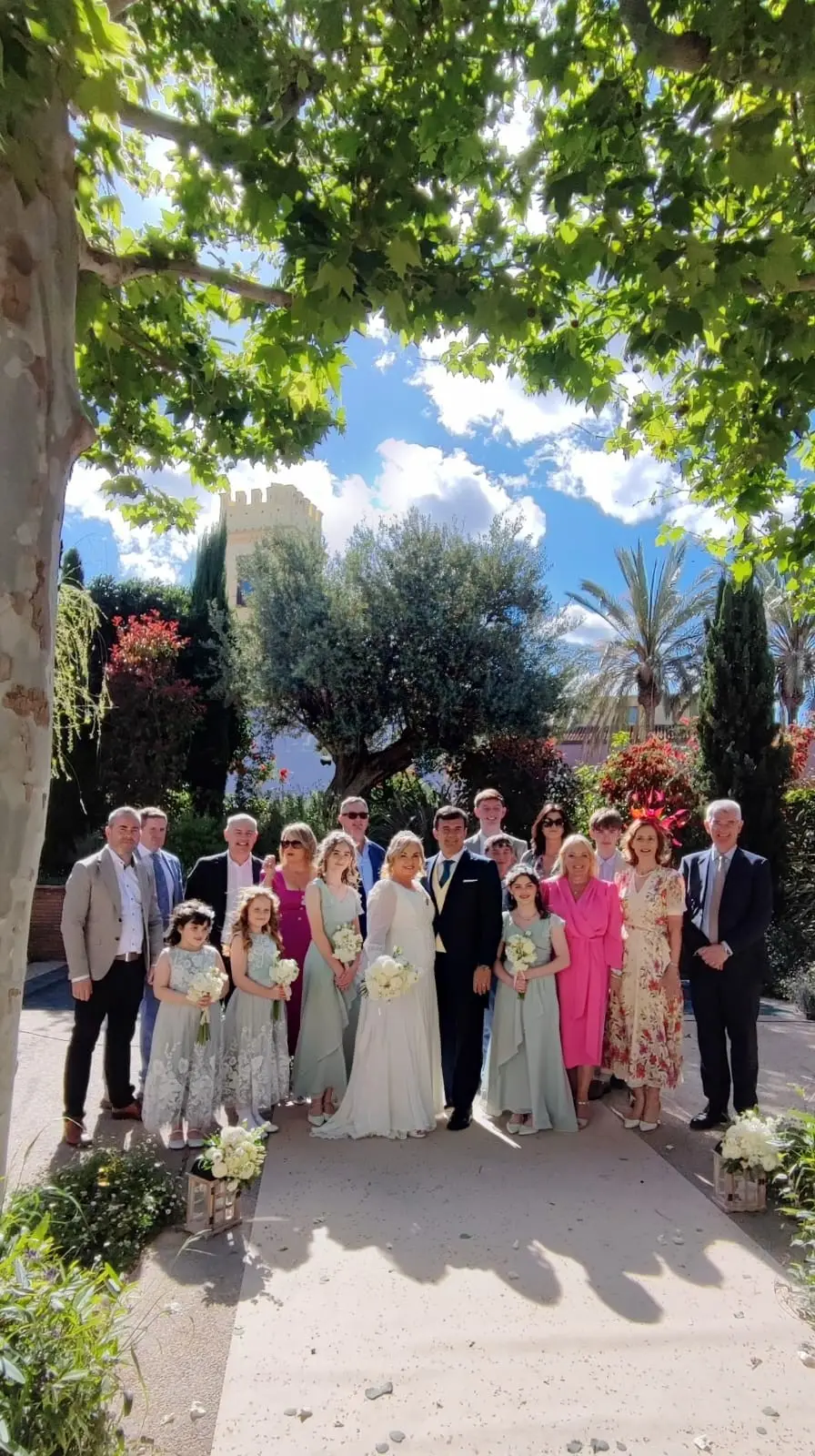 Los novios con sus familias, posando en un camino de grava entre árboles y flores